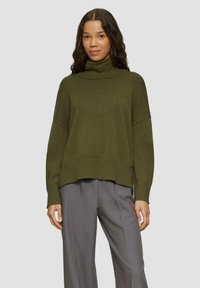 Olive green turtleneck sweater with a relaxed fit, ribbed hem, and wide sleeves, paired with gray wide-leg trousers. Soft knit texture.