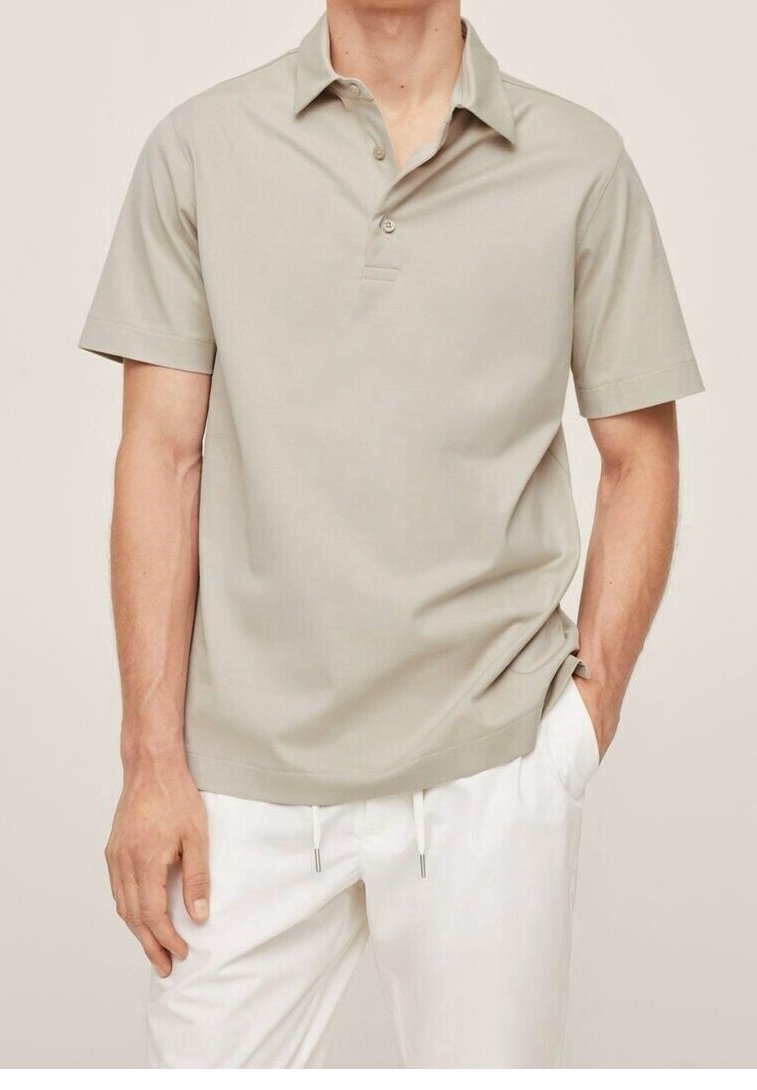 Světle béžová polo košile s krátkým rukávem a límcem, obsahující tři knoflíky a volný střih, spárovaná s bílými kalhotami.