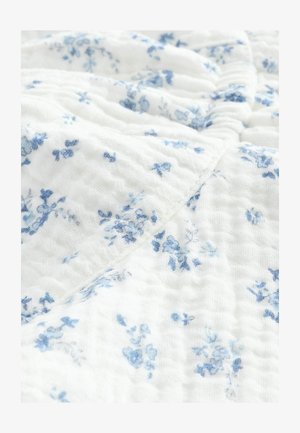 Bela tkanina z teksturirano, gubano površino, z nežnim modrim cvetličnim potiskom, razpršenim po njej.