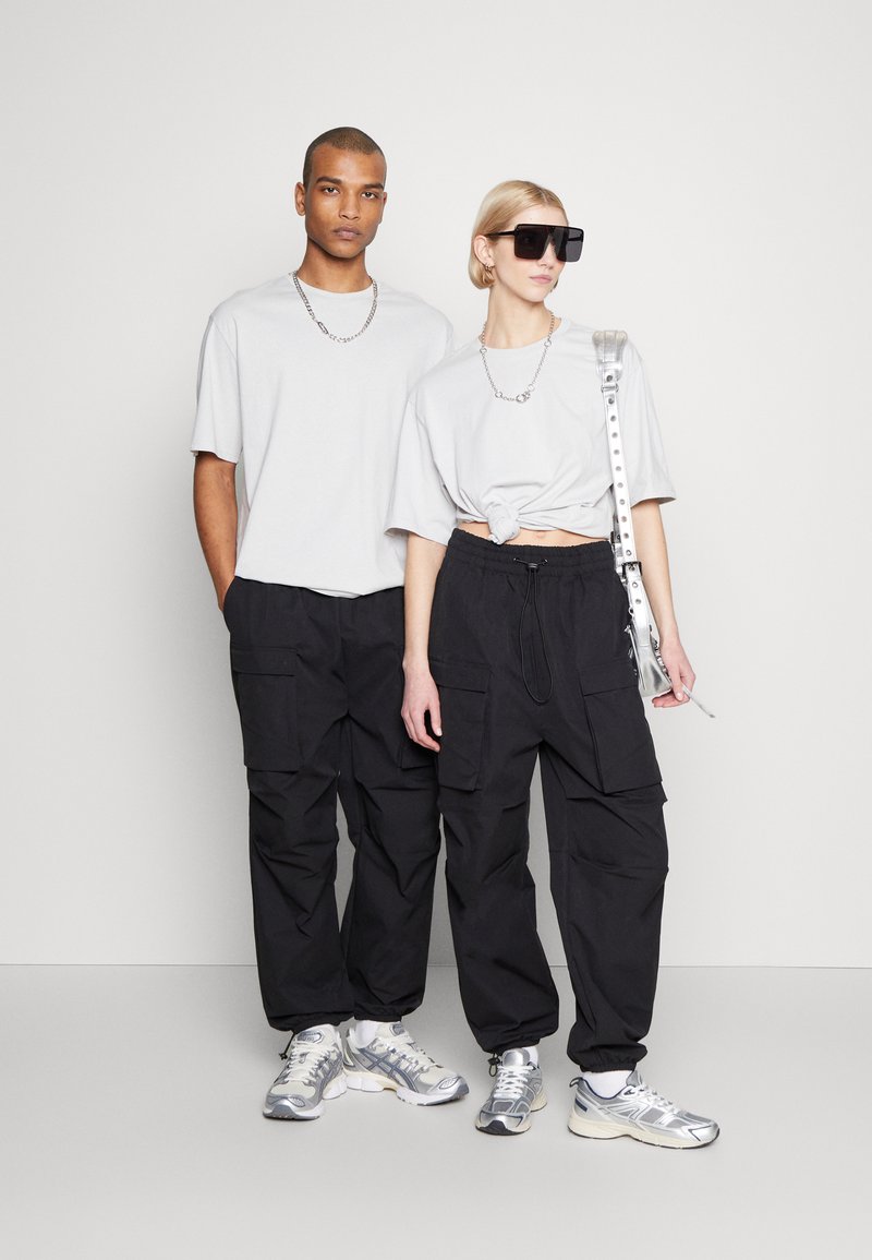 Szürke, oversize pólók, fekete cargo nadrág zsebekkel, ezüst színű sneakers, valamint kiegészítők, mint például nagy napszemüveg és láncnyaklánc.