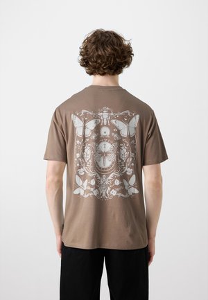 T-shirt en coton brun avec un motif graphique blanc détaillé de papillons et d'insectes dans le dos. Manches courtes et col rond.