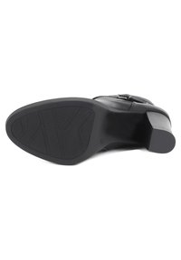 Stivale nero con tacco alto e suola texturizzata, tacco piatto e parte superiore in pelle liscia. Presenta un dettaglio con fascia e fibbia nel design.