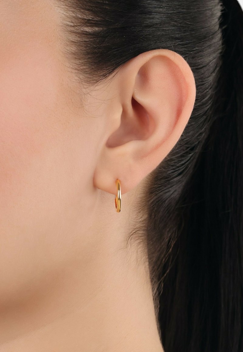 Goldene Creolen, die an einem Ohr präsentiert werden, mit einem eleganten, kreisförmigen Design, einer glatten, glänzenden Oberfläche und einem subtilen Scharnierelement.