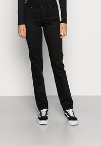 Jeans de mezclilla negra con un diseño de pierna recta. Presentan bolsillos estándar, cierre de botón y están combinados con zapatillas blancas.