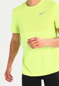Camisa deportiva de manga corta para hombre en tejido de malla amarillo brillante; cuenta con un sutil logo gris de Nike en el pecho. Diseño ligero y transpirable.