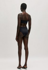 Zwarte bikini set met een eenvoudige bralette bovenstuk met dunne bandjes en een hooggetailleerde onderkant. Gladde, rekbare stof met minimale details.