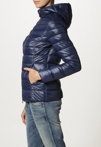 Granatowa kurtka puchowa z kapturem, o poziomym pikowanym wzorze, błyszczącej fakturze i przednich kieszeniach. Zamek błyskawiczny u dołu.