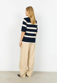 Jūraskrāsas un baltas svītrainas adītas blūzes ar īsām piedurknēm, kopā ar vaļīgām bēšām biksēm. Gluda tekstūra, brīvs piegriezums un vienkāršs dizains.