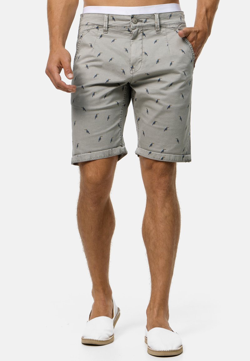 Shorts gris clair avec un motif d'oiseaux discret, fabriqués en coton, dotés d'un ourlet roulé, de poches latérales et d'une fermeture à bouton.