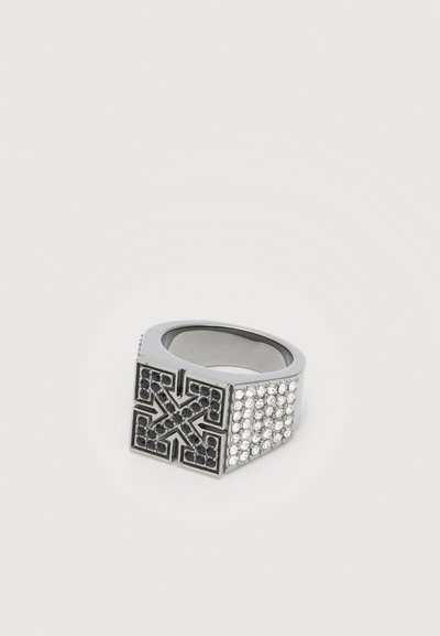 Bague en argent avec un dessus carré présentant un design de croix fléchée noire et des côtés ornés de multiples petits cristaux clairs.