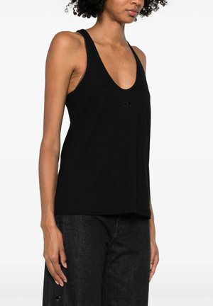 Femme portant un top noir ample sans manches à encolure dégagée et un pantalon noir taille haute sur fond blanc.