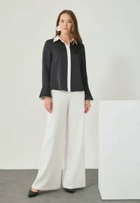 Black and white color-blocked blouse with a pointed collar, paired with wide-leg white pants. Elegant fabric with flared sleeves.