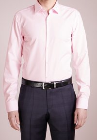 Lichtroze overhemd met een button-down kraag, lange mouwen en een gladde textuur, gecombineerd met donkergekraagde broeken en een zwarte riem.