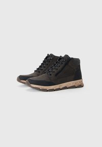 Sneaker alte marroni e nere con suole spesse color beige, lacci neri, cerniera laterale e colli imbottiti contro uno sfondo bianco.