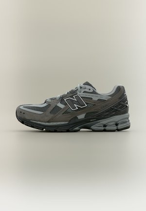 Chaussure de course New Balance homme gris foncé et noir avec tige en mesh et daim, semelle amortissante et logo sur le côté.