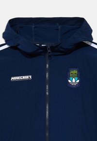 Navy windbreaker with a hood, featuring a zip front and white side stripes. Includes a Minecraft logo and an embroidered Adidas logo.