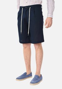 Pantaloni corti blu navy con chiusura a coulisse in materiale misto cotone, dotati di tasche laterali e vestibilità comoda. Abbinati a mocassini blu.