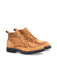 Tan ruskinds ankelboots med rund tå, sort gummisål, snørebånd foran og stofpull-tabs på hælen. Tekstureret overdel med syningsdetaljer.