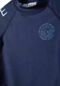 T-shirt de protection solaire bleu marine à manches courtes, arborant un graphique bleu clair d'une planche de surf et le texte "PROFITEZ DE CHAQUE MOMENT, VIBRATIONS DU SOIR."