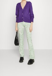 Lila ullkofta med V-ringning och knappar, matchad med gröna marblade tryckade utsvängda byxor samt svart handväska och skor.