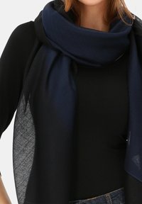 Granatowy szal wykonany z lekkiego materiału, charakteryzujący się miękką, gładką teksturą i luźnym fasonem, noszony na czarnej bluzce.