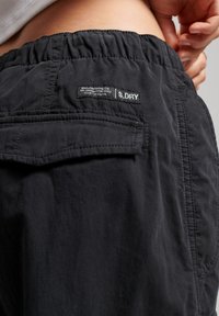 Czarne spodnie cargo z elastycznym paskiem w talii, z kieszonką naszywaną i etykietą S.DRY z tyłu. Materiał jest teksturowany i lekki.