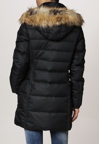 Chaqueta de plumas negra con capucha con borde de piel, presenta un diseño acolchado horizontal, mangas largas y puños texturizados en contraste.