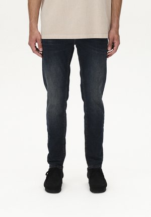Skinny-fit dark blue jeans made of denim, featuring a faded texture and slight wear. Paired with black lace-up shoes.
