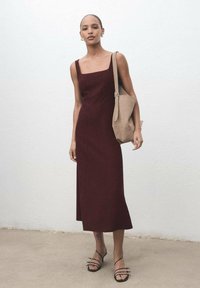 Bordeaux midi-jurk met een vierkante halslijn en slanke bandjes. Gepaard met een beige tote bag en zwarte sandalen met bandjes. Glad stof textuur.