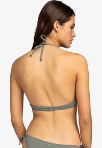 Grön bikinitopp med halterneck och bakfäste. Slät textur med justerbara band vid hals och rygg. Minimalistisk design.