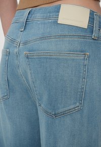 Světlé modré džíny z denimu s vysokým pasem, dvěma zadními kapsami a koženou značkovou nášivkou na pásku. Jemná textura s minimálním šitím.