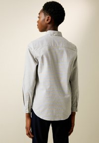 Kockás ing kék, zöld és fehér színekben, gombos gallérral és hosszú ujjakkal. Könnyű anyag, sima textúrával.