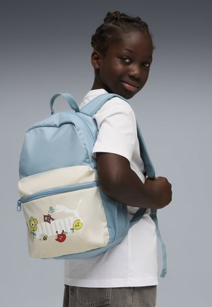 Mochila de tela azul claro con fondo crema, con gráficos coloridos de flores y frutas, bolsillo con cremallera y correas ajustables.