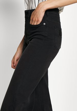 Calças jeans de ganga preta de perna larga com cintura alta, bolso frontal e bolso aplicado nas costas. Textura suave com detalhes de costura minimalistas.