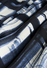 Close-up van stof met abstracte rechthoekige patronen in zwart, wit en blauw, met zichtbare gevouwen en gestructureerde textieloppervlakte.