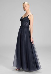 Granatowa suknia wieczorowa z wymyślnym haftem na przezroczystym topie, cienkimi ramiączkami i zwiewną spódnicą z tiulu. Srebrne sandały na obcasie.