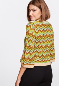 Sweter w formie kardiganu z wielokolorowym wzorem chevron w odcieniach zieleni, żółci, brązu i brzoskwini; rękawy o długości trzech ćwierć; wykończony beżowym paskiem.
