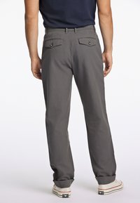 Chinos gris avec une coupe droite, deux poches arrière avec fermetures à bouton et ourlets retroussés, associés à des baskets blanches.