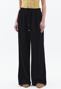 Pantalones de pierna ancha negros, hechos de una tela ligera, con una cinturilla elástica y cordón, diseñados para un ajuste relajado.