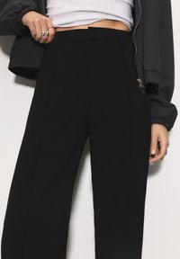 Čierne nohavice s vysokým pásom z hladkej látky, s priliehavým strihom, čistými líniami a bočnými vreckami. Na páse so zipsom.
