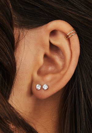 Boucle d'oreille en or et boucles d'oreilles claires en zircon cubique rond sur une oreille percée. Texture lisse, surfaces brillantes et design simple.