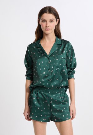 Completo pigiama in raso verde composto da una camicia con bottoni e tasca e pantaloni corti, entrambi decorati con un motivo floreale.
