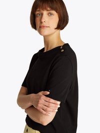 Black short-sleeve top featuring a boat neckline, button accents on the shoulder, and a fitted design. Soft, smooth fabric texture.