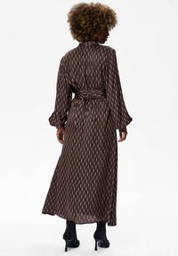 Brązowa maxi sukienka w wzory z długimi rękawami i paskiem w talii, z pionowymi liniami w odcieniach brązu i subtelną fakturą.