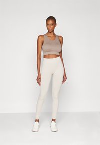 Top atlético corto de color marrón claro con una textura suave, combinado con leggings crema que presentan un diseño acanalado. Zapatillas blancas completan el atuendo.