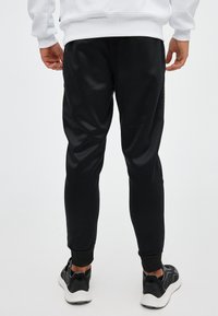 Pantalones jogger negros con un ajuste cónico, con puños elásticos y una textura suave. Combinados con zapatillas deportivas negras y blancas.
