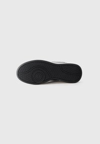 Sole in gomma nera di una sneaker con battistrada testurizzato e dettaglio del logo circolare centrato su uno sfondo bianco uniforme.