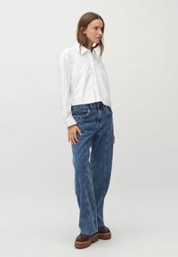 Camicia bianca a maniche lunghe con bottoni, abbinata a jeans in denim blu con vita arricciata e scarpe con piattaforma marroni. Design semplice.
