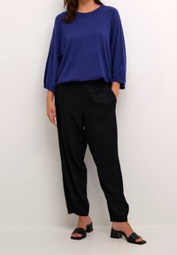 Texturiertes, navyblaues Oversized-Pullover mit überschnittenen Schultern, kombiniert mit schwarzen, taillierten Hosen und schwarzen, hohen Sandalen. Schlichtes und modernes Design.
