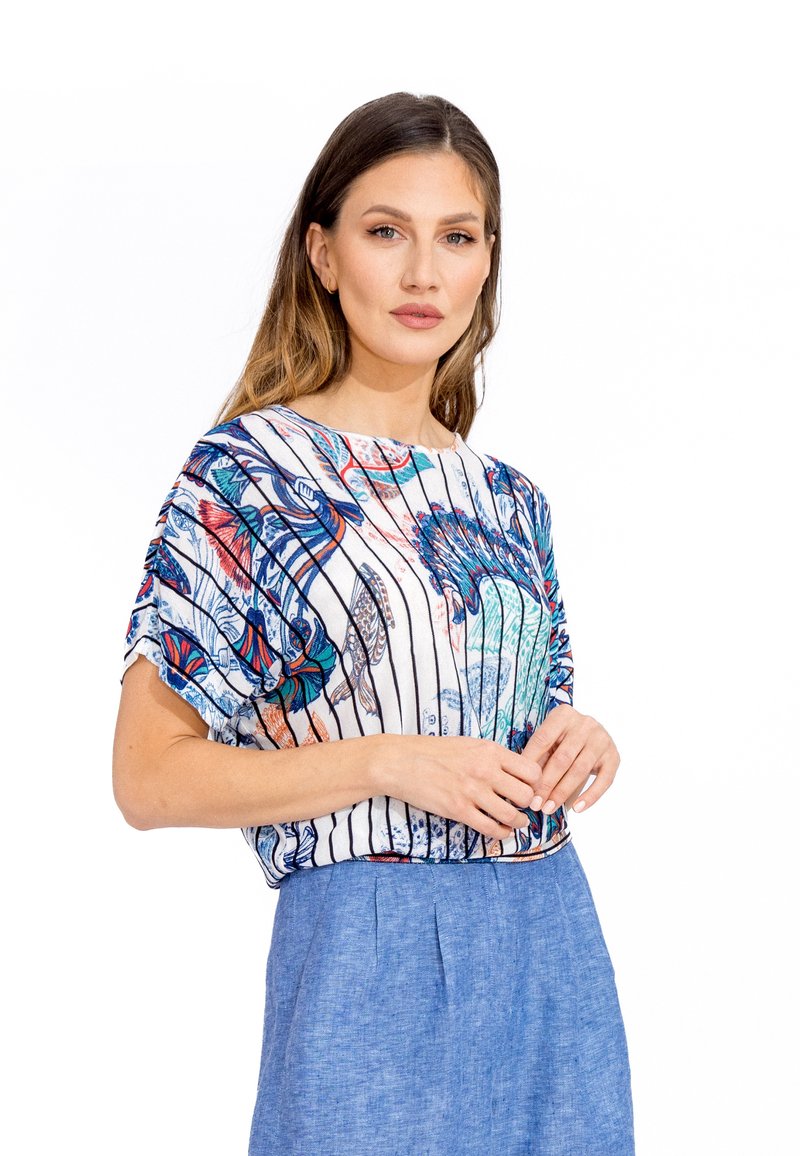 Bloemmotief blouse met blauwe, rode en groene ontwerpen op een witte gestreepte achtergrond. Losse pasvorm met korte mouwen, gecombineerd met een blauwe rok.